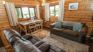 L’intérieur d’un chalet en bois, avec un canapé, une table à manger et des chaises, ainsi qu’une fenêtre avec des rideaux.