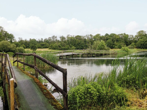 A wooden bridge over a calm body of water, surrounded by lush greenery and a paved walkway. - Oak Lodge (Llanelli)