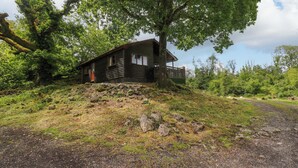 Une cabane dotée d’un porche, entourée d’arbres et bordée d’un chemin de gravier.