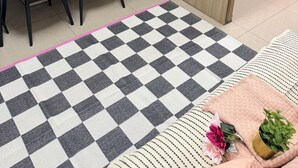 Une chambre moderne avec un coin repas, un lit avec une literie rose, un tapis à carreaux et un téléviseur diffusant une scène de la nature.