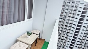 Un balcon avec une table et des chaises, une vue sur un immeuble de grande hauteur et un espace recouvert d’un gazon artificiel.