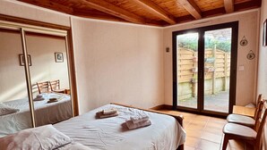 A bedroom with a large bed, a wooden ceiling, a sliding glass door to a patio, and a small table with chairs. - The Saint Colomban house (Carnac)