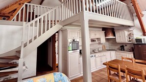 A spacious loft with a wooden staircase, a dining area, and a kitchen. - The Saint Colomban house (Carnac)