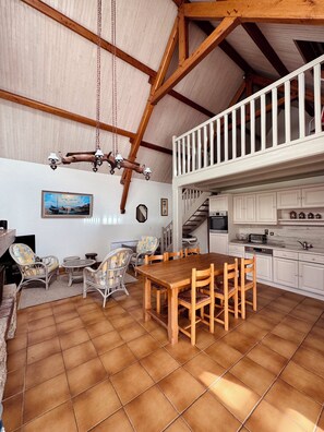 A spacious dining area with a wooden table and chairs, a hanging chandelier, and a white staircase leading to an upper level.