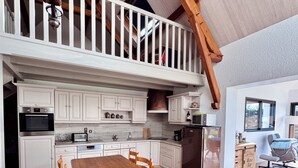 A spacious kitchen with white cabinets, a wooden dining table, and a high ceiling with exposed beams. - The Saint Colomban house (Carnac)
