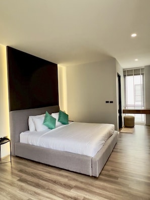 Una habitación de hotel moderna con una cama grande, cabecera y piso de madera.