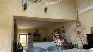 Een eethoek met een tafel gedekt voor twee personen, een vaas met bloemen en een rustieke keuken op de achtergrond.