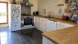Een compacte keuken met een koelkast, oven en vaatwasser, een houten aanrechtblad en een betegelde vloer.