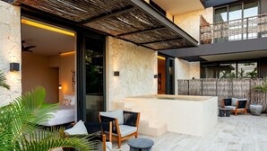 A modern outdoor living area with stone walls, a hot tub, and outdoor seating. - Bloom Tulum | 4-BR Apartment | w/ Fully Equipped Kitchen + Pool (Tulum)