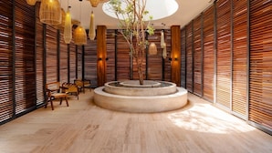 A modern interior with wooden slatted walls, a central circular planter with a tree, and multiple hanging light fixtures.