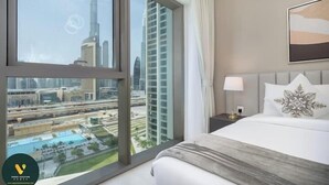A hotel room with a large window offering a view of a cityscape, including a tall skyscraper. - Vogue | Downtown with Direct Access to Dubai Mall (Dubai)
