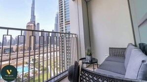 A balcony with a view of the Burj Khalifa and other buildings, a gray sofa, a small table with a plant, and a decorative wall panel. - Vogue | Downtown with Direct Access to Dubai Mall (Dubai)