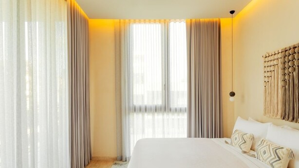 A modern hotel room with a large bed, sheer curtains, and a warm ambient light.