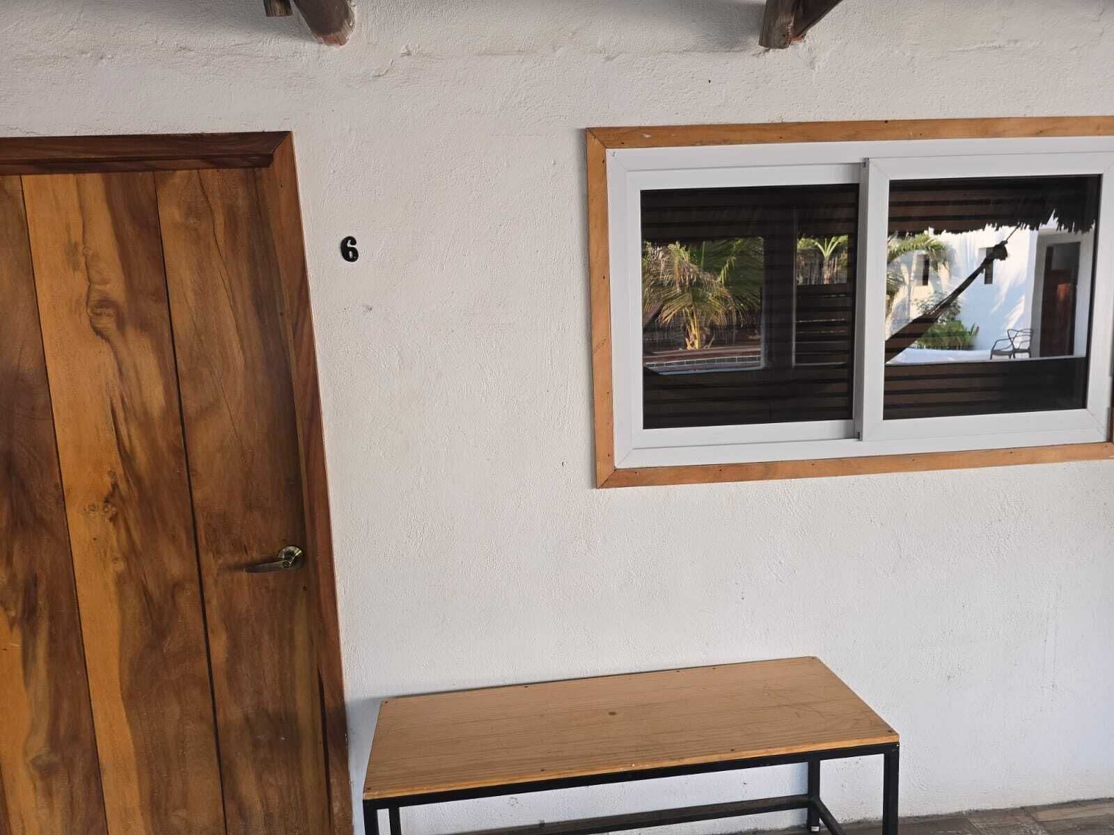 A wooden door, a small table, and a window with a view of palm trees and a house.