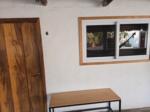 A wooden door, a small table, and a window with a view of palm trees and a house. - Hot Chipilin El Paredon (Sipacate)