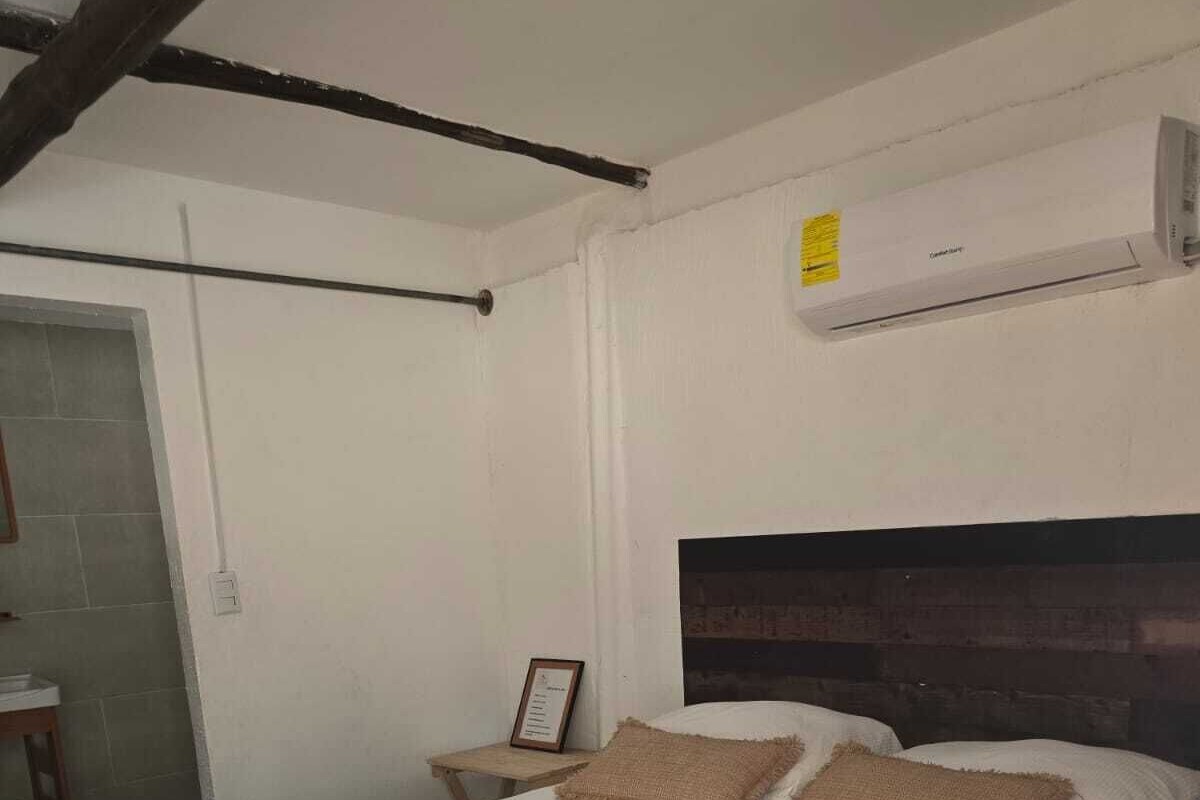 Un dormitorio con cama, mesita de noche, un cuadro enmarco y un equipo de aire acondicionado.