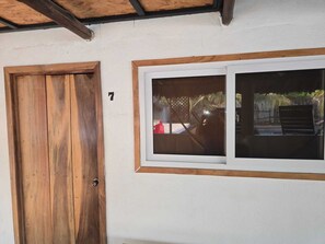 A wooden door with a number 7, a window with a view of a garden, and a white wall. - Hot Chipilin El Paredon (Sipacate)