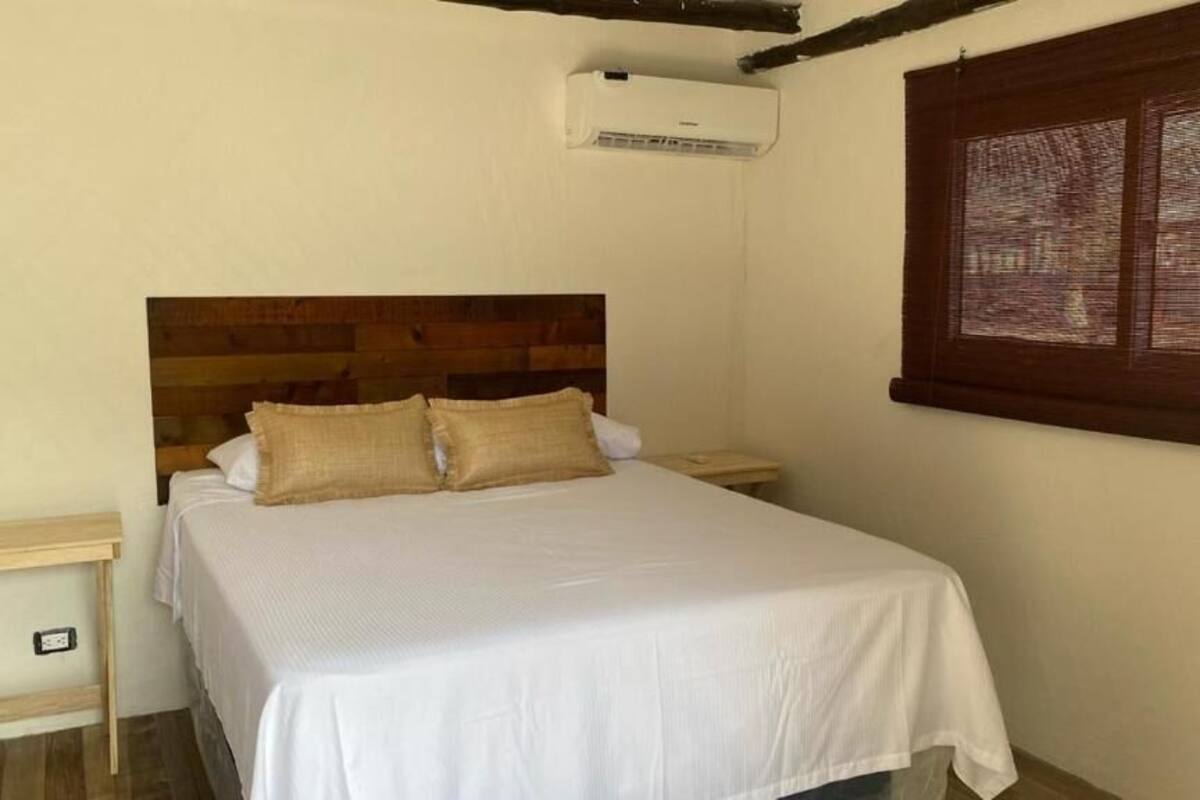 Una cama individual con cabecera de madera, una mesita de noche y una ventana con persianas.