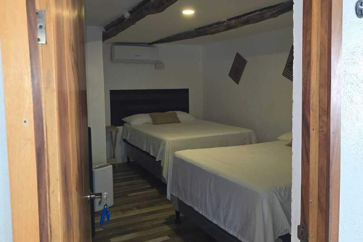 Una habitación con dos camas, suelo de madera y techo con vigas a la vista.