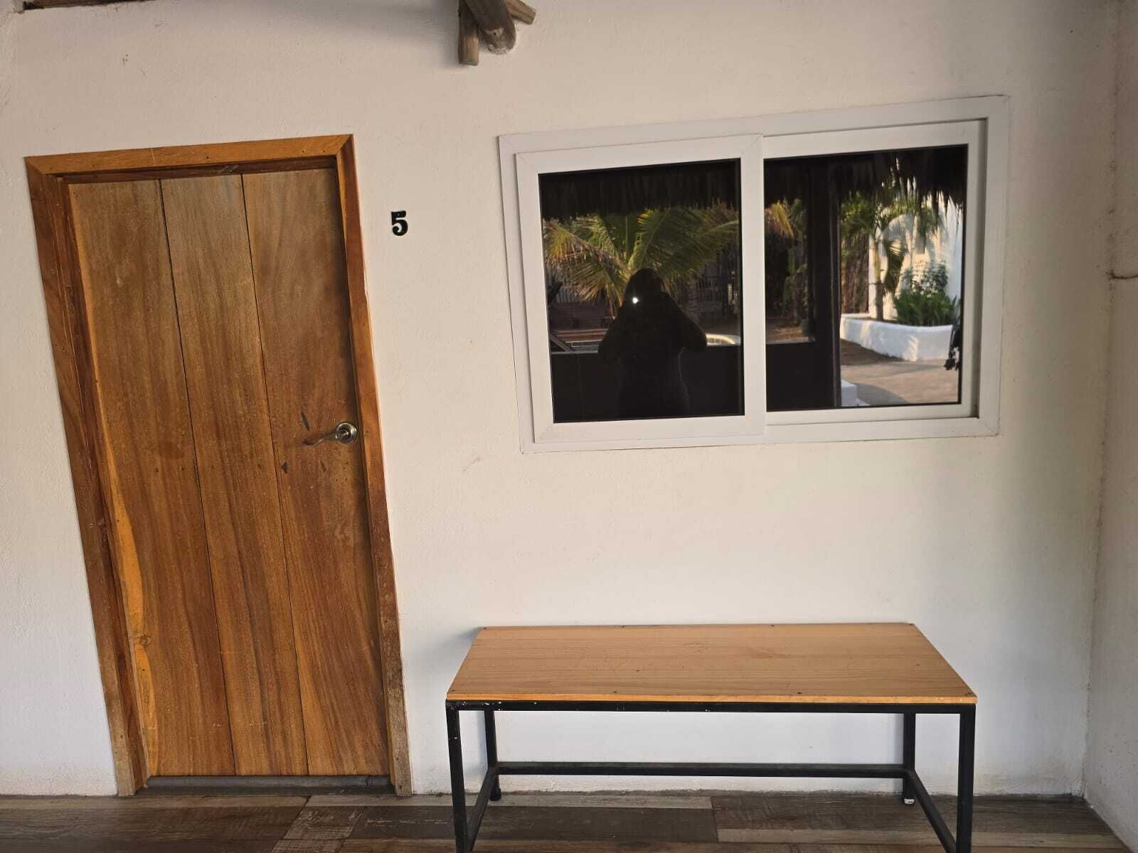 Una habitación con puerta de madera, un banco y ventana con vista a palmeras.