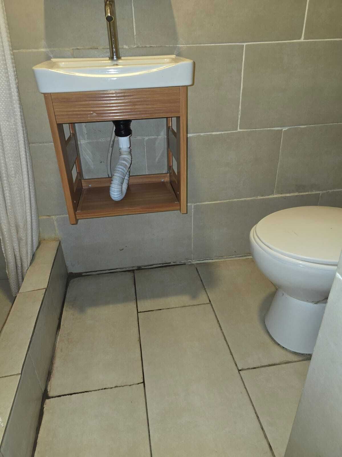 A bathroom with a white toilet, a wooden vanity with a sink, and a shower area.