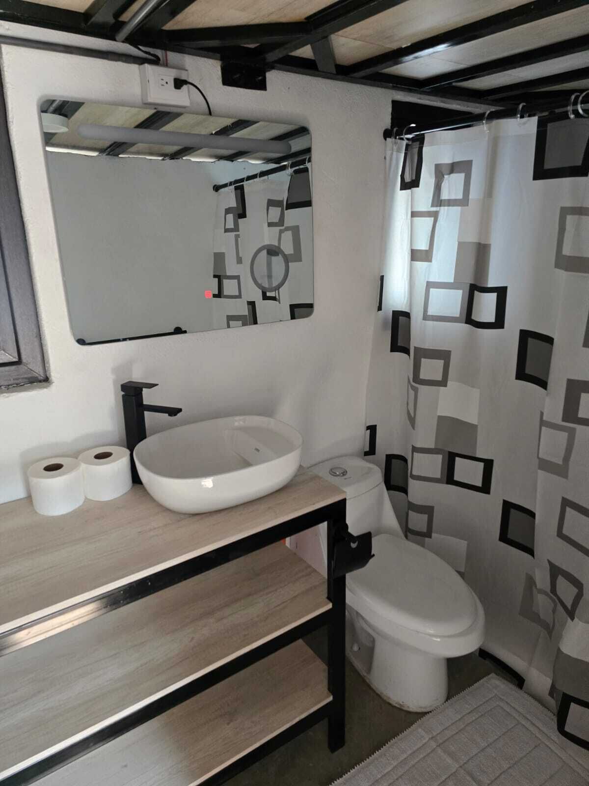 A bathroom with a white sink, black faucet, toilet, and a shower curtain with a geometric pattern.