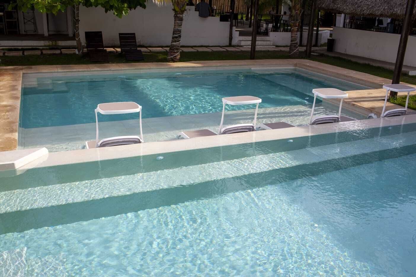 Una piscina rectangular con agua cristalina, rodeada por un solárium blanco.