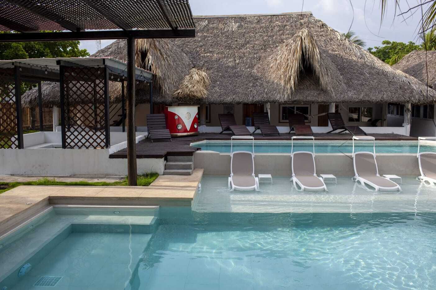 A pool area with lounge chairs, a thatched-roof structure, and a red and white object.