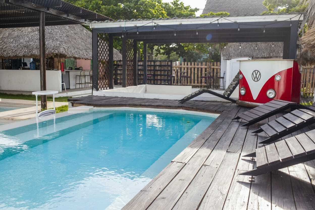 A swimming pool with a wooden deck, a thatched-roof structure, and a VW camper.