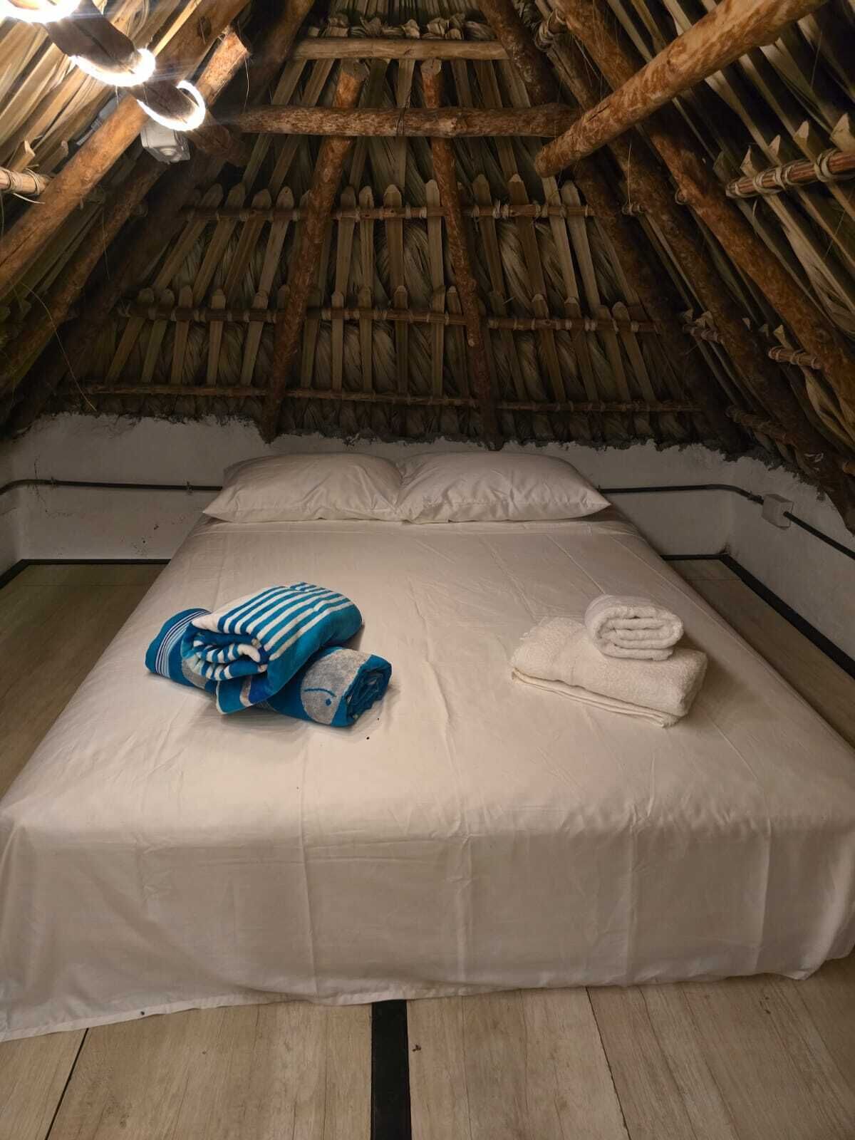 A room with a thatched roof, a bed with white linens, and a blue striped blanket.