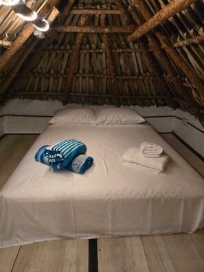 Une pièce avec un toit de chaume, un lit recouvert de draps blancs et une couverture à rayures bleues.