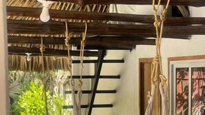 A hammock suspended from a wooden ceiling in a room with a thatched roof and a view of greenery outside. - Hot Chipilin El Paredon (Sipacate)