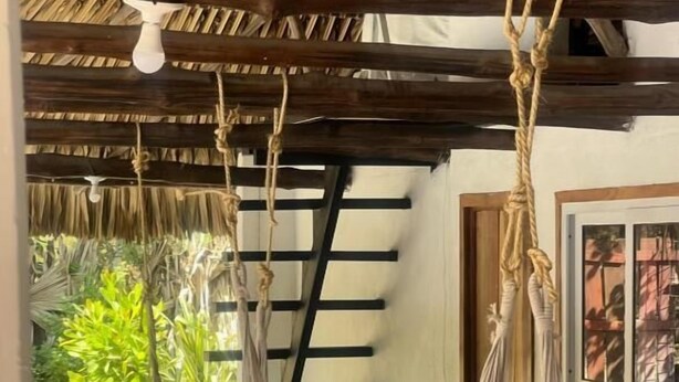 A hammock suspended from a wooden ceiling in a room with a thatched roof and a view of greenery outside. - Hot Chipilin El Paredon (Sipacate)