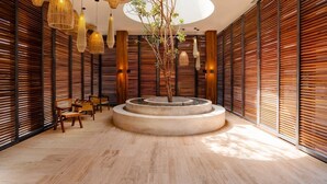 A modern interior with wooden slatted walls, a central circular planter with a tree, and multiple hanging light fixtures. - Two 1-BR 1 King | Bloom Tulum | w/ Fully Equipped Kitchen +  Pool (Tulum)