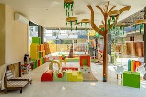 Zona de juegos infantiles con estructuras de colores y un área de descanso con cojines a rayas.