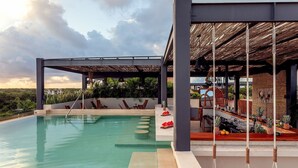 Uma área de piscina com espreguiçadeiras, um bar e uma área de estar coberta com telhado de palha.