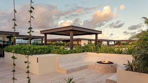 Um jardim no terraço com pérgola, lareira e diversas plantas.