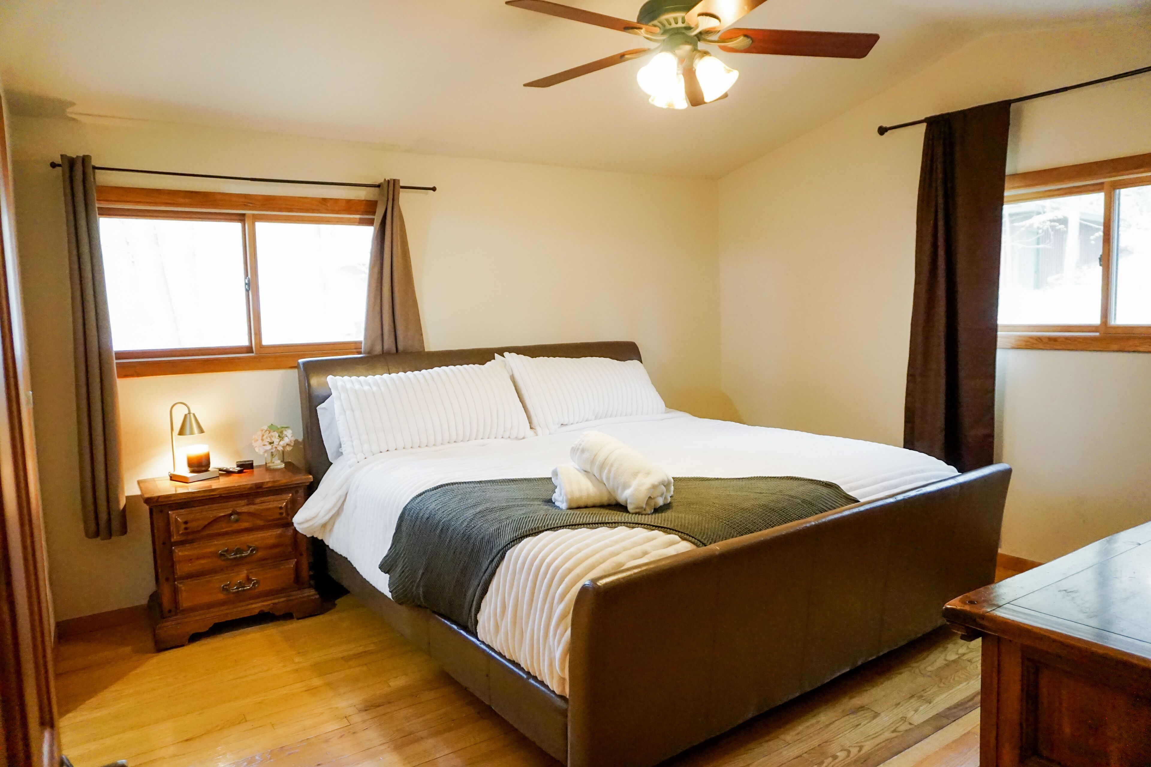 A bedroom with a bed, wooden nightstand, bedside lamp, and a ceiling fan.
