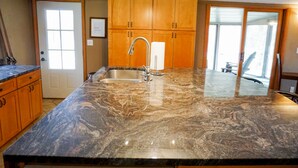 A kitchen with a granite countertop, stainless steel sink, wooden cabinets, and a view through a glass door. - Rib Mountain Cabin (Wausau)
