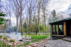 A rustic cabin with a porch, a hot spring, and a forested backdrop.
