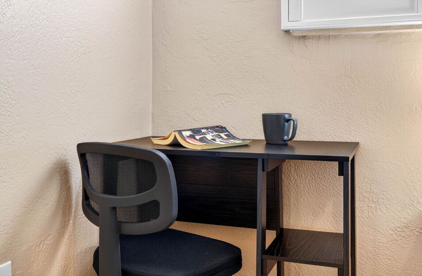 Un escritorio pequeño y oscuro con una silla, un libro y una taza.