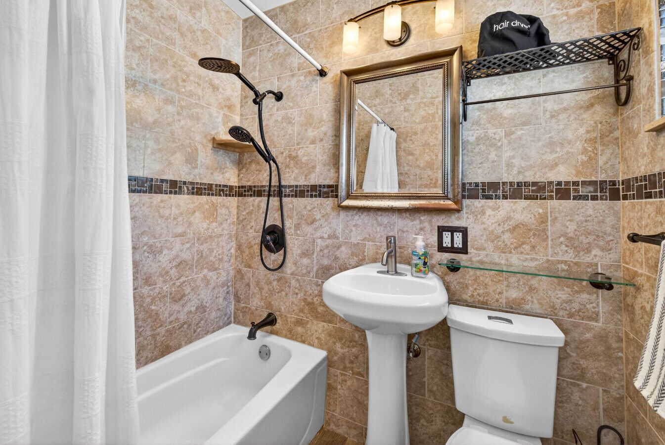 A bathroom with a bathtub, a sink, and a toilet. There is a showerhead, a mirror, and a towel rack.