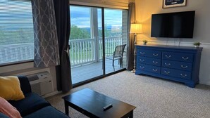 En stue med sofa, sofabord, fjernsyn og en balkon med udsigt.