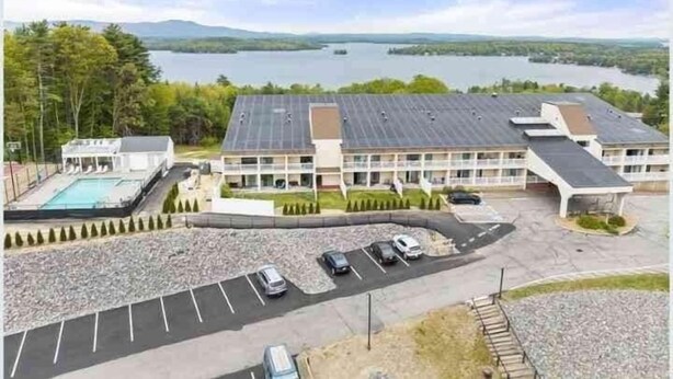 Hotel med swimmingpool, parkeringsplads og udsigt til en sø.