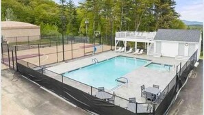 En swimmingpool med basketballbane, liggestole og et overdækket siddeområde.