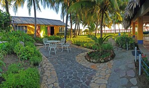 Un patio empedrado con una mesa y sillas, rodeado de abundante follaje y palmeras.