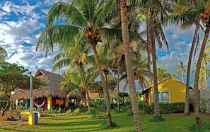 Ein tropisches Resort mit strohgedeckten Hütten, Palmen und einem gelben Gebäude.