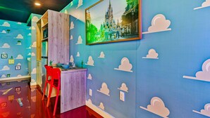 Ein Zimmer mit blauer Wand, die Wolkenmuster zeigt, einem gerahmten Bild eines Schlosses, einem roten Sessel und einem Holzschrank.