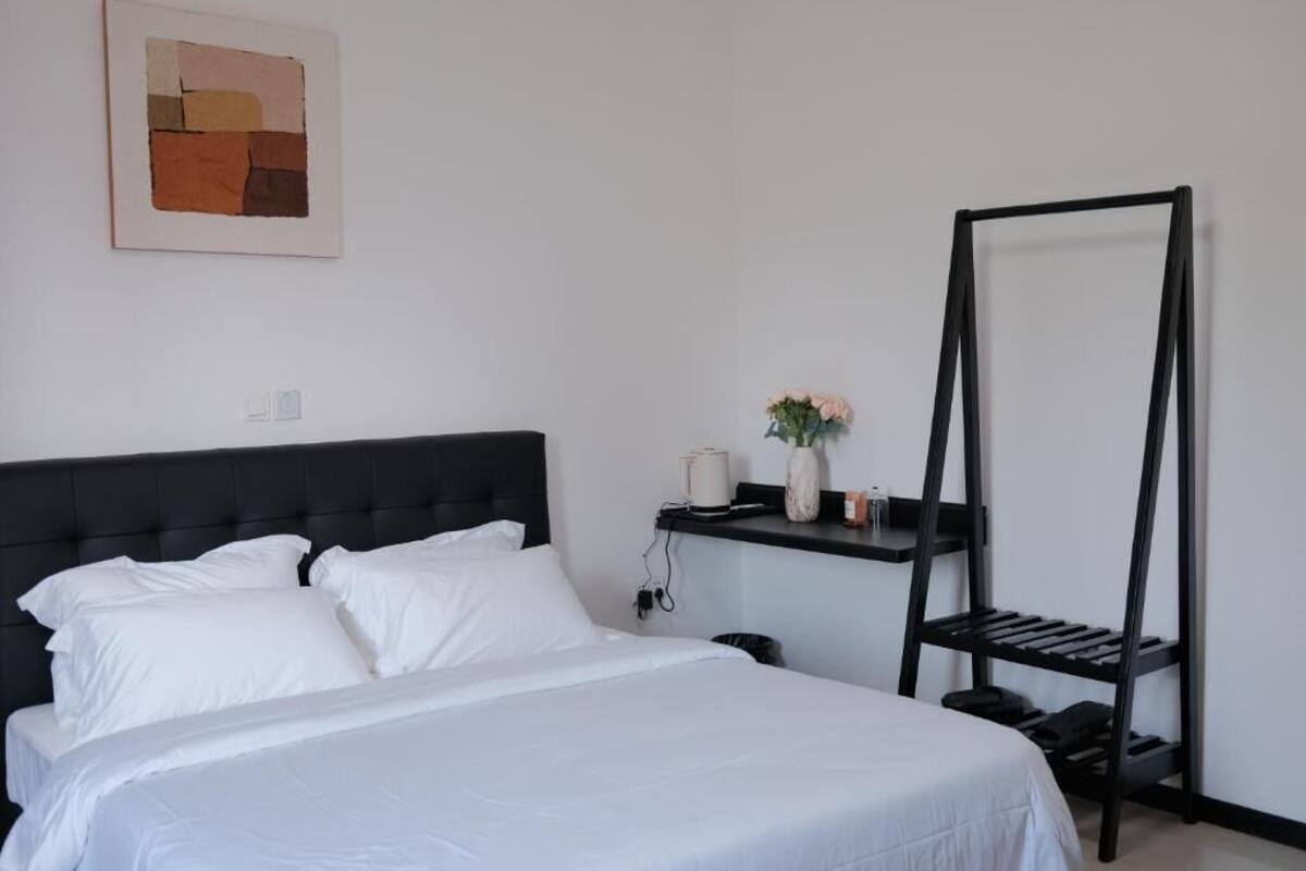 Un lit bien fait, avec du linge de lit blanc, une tête de lit noire et un tableau abstrait accroché au mur.