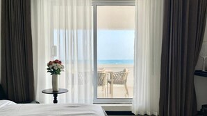 Ein Hotelzimmer mit Bett, einem kleinen Tisch mit Blumenvase und einem Balkon mit Blick auf den Strand.